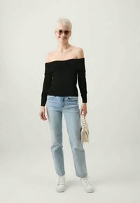 Svart off-shoulder topp, lange ermer, myk stoff; lyseblå rette jeans; hvite sneakers; holder en beige håndveske.