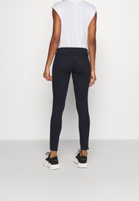 Mörkblå tajta jeans i denim med midjemodell, smal passform och bakfickor. Kombinerade med en vit t-shirt och svarta sneakers.