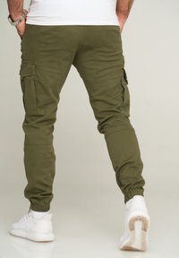 Olive green cargo pants with elastic cuffs, multiple side pockets, and a fitted design. Made of stretchable fabric, showcasing a smooth texture.