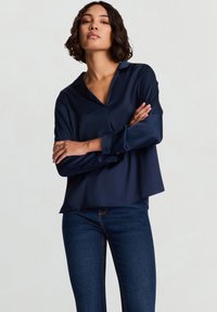 Chemise en satin bleu marine avec col, manches longues et coupe décontractée ; dotée d'une fermeture par boutons et d'une texture lisse et brillante.
