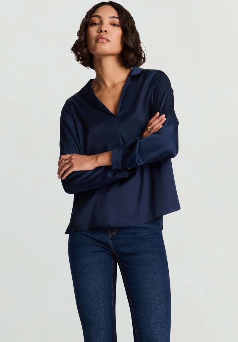 Chemise en satin bleu marine avec col, manches longues et coupe décontractée ; dotée d'une fermeture par boutons et d'une texture lisse et brillante.