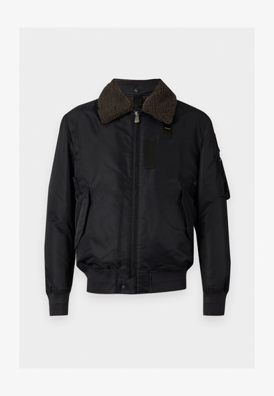 Blouson bomber noir avec col en shearling marron doux, fermeture éclair frontale, deux poches latérales et poignets et ourlet côtelés.