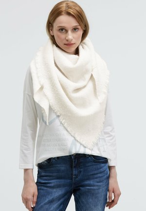 Large, triangular cream scarf made of soft, textured fabric with fringed edges, worn over a light-colored long-sleeve shirt.
