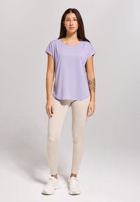 Lichtpaarse top met korte mouwen en een relaxte pasvorm, gecombineerd met beige leggings en witte sneakers. Glad textuur, casual ontwerp.