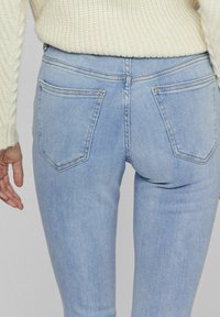 Jeans ajustados de color azul claro, hechos de mezclilla, que presentan dos bolsillos traseros, costuras sutiles y un acabado suave, combinados con un suéter de punto crema.