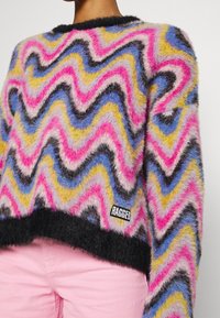 Maglione corto colorato con motivo zigzag in rosa, nero, blu e giallo. Realizzato in materiale morbido con bordi neri e etichetta del marchio.