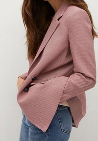 Punavalkoruudullinen räätälöity bleiseri, jossa on lovikaulus, kaksirivinen napitus ja pidennetyt hihat, yhdistetty farkkuihin.