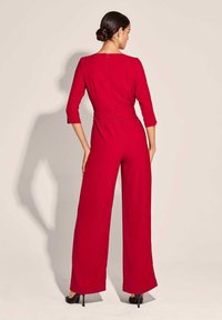 Rode jumpsuit met driekwart mouwen, wijde benen en een fitted taille. Heeft een ritssluiting op de rug en een soepele stof.