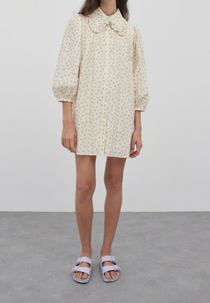 Květinové krátké šaty s nafouknutými rukávy, velkým límcem a knoflíky vpředu. Světle krémová látka s malými oranžovými a hnědými květy.