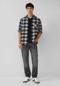 Czarna i biała w kratę flanelowa koszula, podwinięte rękawy, zestawiona z czarnym t-shirtem, szarymi dżinsami i białymi trampkami z czarnymi akcentami.