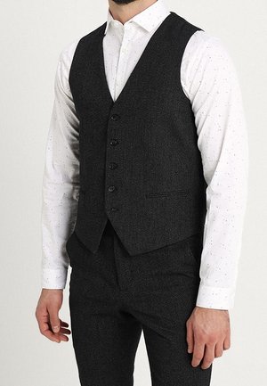 Dunkelgraue Wollweste mit fünf Knöpfen und schmalen Revers, getragen über einem weißen Hemd mit schwarzen Sprenkeln. Verfügt über seitliche Taschen und eine taillierte Passform.