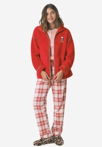 Czerwona puszysta kurtka z zamkiem błyskawicznym z motywem Snoopy, w połączeniu z czerwono-białymi spodniami od piżamy w kratę. Całość uzupełniają kapcie w leopardzi wzór.