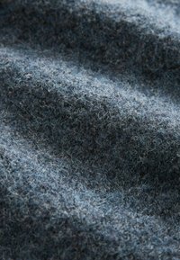 Tissu en laine bleue avec une texture duveteuse, présentant un mélange de teintes plus foncées et plus claires, montrant des fibres naturelles et de subtiles variations dans le tissage.