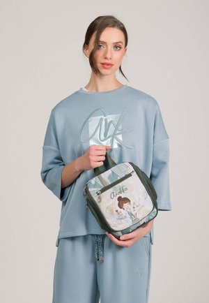 Mujer con atuendo informal azul claro sosteniendo una bolsa de almuerzo cuadrada aislada con una niña de dibujos animados y texto en el frente.