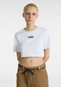Hvid cropped t-shirt med sort "VANS" logo i midten. Korte ærmer og lavet af bomuldsstof. Båret med brune bukser med knapdetaljer.