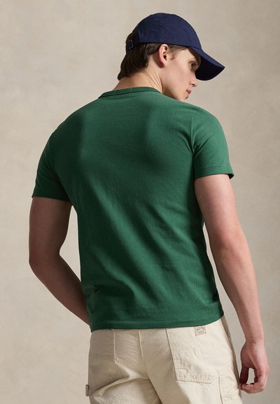 Πράσινο βαμβακερό T-shirt με κοντά μανίκια, εφαρμοστή γραμμή, στρογγυλή λαιμόκοψη, συνδυασμένο με μπεζ cargo σορτς. Όψη από πίσω που δείχνει απαλή υφή.