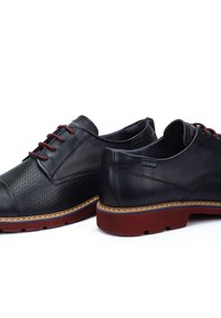 Chaussures en cuir noir avec un design perforé et des accents bordeaux. Bout arrondi, semelle extérieure en brun avec traction en caoutchouc et détails de couture contrastants.