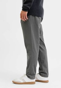 Graue Jogginghosen mit einem elastischen Bund, Seitentaschen und einer lockeren Passform, kombiniert mit weißen Sneakers mit beigen Akzenten.