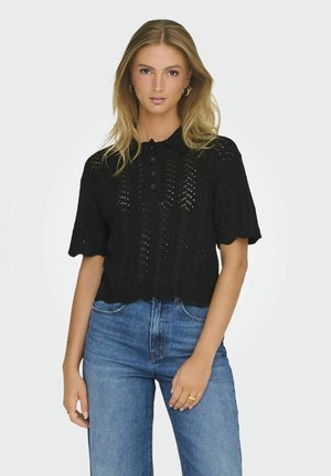 Polo noir en maille, à manches courtes, avec fermeture par boutons et ourlet en dentelle, associé à un jean bleu taille haute.