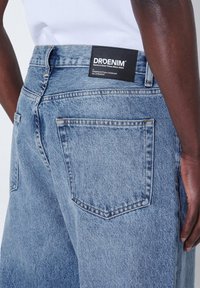Jeans de mezclilla de color azul claro con corte recto, que presentan bolsillos traseros y una etiqueta negra con la marca "DRDENIM". Diseño clásico de cinco bolsillos.