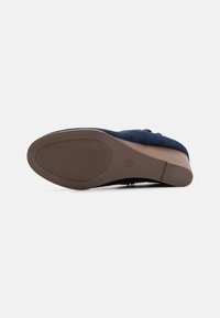 Chaussure compensée en suède bleu vue du dessous, montrant une semelle en caoutchouc brun, taille 37, et un talon en bois.
