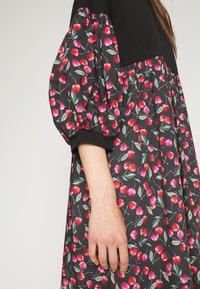 Czarna sukienka z bufiastymi rękawami, ozdobiona wzorem wiśni i liści na ciemnym tle. Miękka tkanina z elastycznymi mankietami.