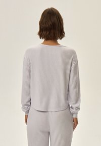 Jasnofioletowa, prążkowana bluzka z długim rękawem, o okrągłym dekolcie i ściągniętych rękawach, pokazana z tyłu z dopasowanymi prążkowanymi spodniami.