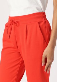 Röda joggarbyxor med elastisk midja, snörning och två sidfickor. Tyget ser slätt ut med en lätt glans.