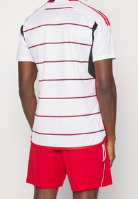 White short-sleeve sports jersey featuring red horizontal stripes and black side accents, paired with red shorts. Smooth texture, athletic fit.