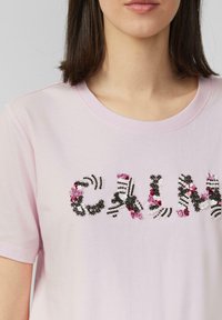 T-shirt en coton rose avec "CALM" brodé en relief, agrémenté de motifs floraux et de sequins. Col rond et manches courtes.