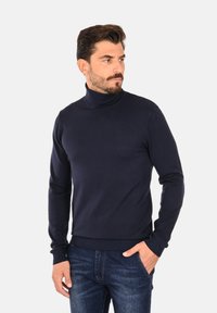 Maglione a collo alto di colore navy realizzato in materiale lavorato a maglia, con maniche lunghe e polsini a costine, abbinato a jeans blu.