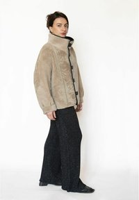 Beige fluffy jakke med høj krave, sorte knapper og kontrasterende sort kant, kombineret med løse sorte teksturerede bukser og sorte sko.