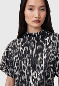 Top de patrón en blanco y negro con cuello alto y mangas cortas, que presenta una tela suave y fluida con un estampado similar al de un leopardo.