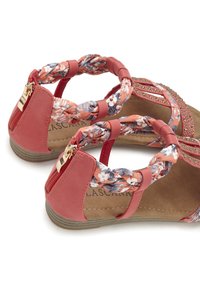 Koraal kleurige sandalen met gevlochten bloemenbandjes, een gevoerde binnenzool en een kleine gouden rits. Geprofileerde rubberen buitenzool met een platte zool.
