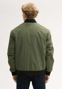 Olivgrön bomberjacka med svart krage och manschetter, tillverkad av ett slätt, lättviktigt tyg och med en avslappnad passform. Inga synliga mönster eller hårdvara.