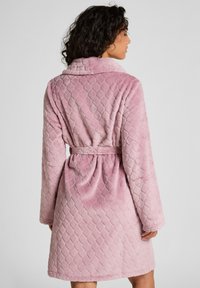 Rosa, gesteppter Bademantel aus weichem, plüschigem Stoff. Verfügt über einen Schalkragen und einen Bindegürtel in der Taille, hat lange Ärmel und einen knielangen Schnitt.
