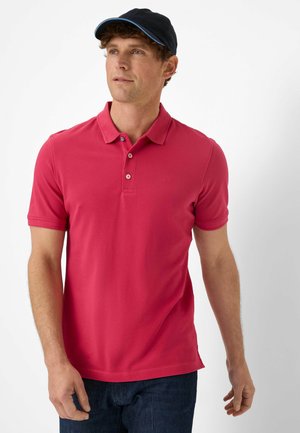 Rode polo met een kraag, korte mouwen en een logo. Draagt bij donkere denim jeans en een marineblauwe pet met een lichtblauwe accent.