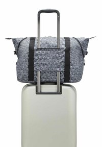 Borsa da viaggio a motivo bianco e nero con doppi manici neri appoggiata su una valigia rigida grigio chiaro, dotata di maniglia telescopica.