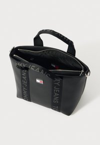 Mustast sünteetilisest materjalist kott, millel on tõmblukuga sulgemine, kaks lühikest käepidet ja dekoratiivne rihm, millel on kiri „TOMMY JEANS“. Siseküljel taskud.