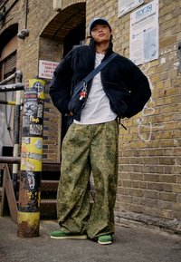 Μαύρο καπιτονέ μπουφάν, λευκό μπλουζάκι, πράσινα καμπάνα παντελόνια με σχέδιο και πράσινα παπούτσια. Αξεσουάρ περιλαμβάνουν ένα τσάντα χιαστί και ένα μπλε καπέλο.