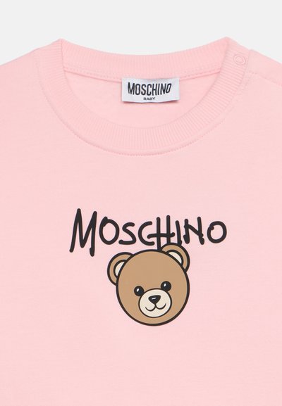Светлорозова бебешка риза с лого на Moschino и карикатурно мече отпред под текста.