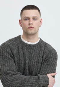 Mørk grå, ribbestrikket genser med rund hals og lange ermer, laget av mykt, strukturert stoff. Brukt over en hvit skjorte.