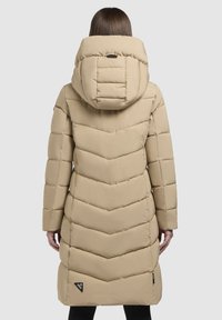 Manteau matelassé beige avec une capuche profonde, motif en chevrons et un patch logo sur l'ourlet. Fabriqué en matériau lisse et léger.