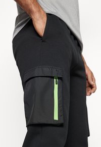 Zwarte cargobroek met een zijzak met een groene ritssluiting, een gladde textuur en een strak design. Geschikt voor casual wear.