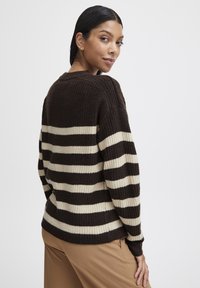 Maglione a righe marroni e crema con texture a coste, caratterizzato da una vestibilità ampia e spalle scese. Orlo leggermente curvo e maniche lunghe.