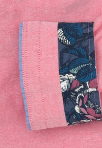 Roze shirtstof met een gestructureerde weving, voorzien van een met bloemenpatroon versierde manchet in marineblauw, afgewerkt met lichtblauwe rand.