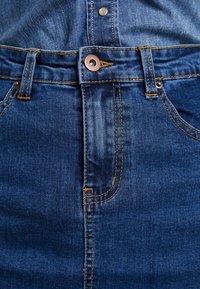 Denimrock in Dunkelblau mit bronzefarbenen Knöpfen, orangen Nähten und einer hoch geschnittenen, figurbetonten Passform.