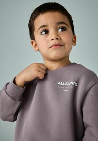 Violetajam džemperim ir ribotām aprocēm un kakla izgriezumu, uz kura priekšpuses ir balta teksts ar "ALLSAINTS" logo. Gluda tekstūra.