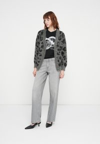 Grå leopardmønstret cardigan med fuzzy tekstur, knaplukning, båret over en sort grafisk T-shirt og grå vide bukser, parret med sorte hæle.
