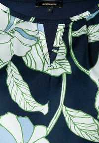 Bluse mit Blumenmuster, V-Ausschnitt, navyblauem Hintergrund und grünen sowie blauen Blättern. Aus glattem, strukturiertem Stoff gefertigt.